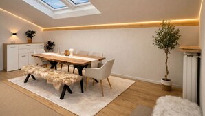 Een moderne eethoek met dakraam, houten tafel, witte stoelen en een potplant.