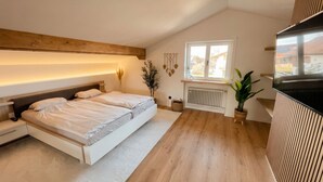 Een moderne slaapkamer met een groot bed, nachtkastjes, een radiator, een raam en een potplant.