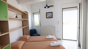 Ein Hotelzimmer mit zwei Betten, einem grünen Schrank, einem blauen Sessel, einem Fenster und einer Tür.
