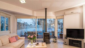 Ein modernes Wohnzimmer mit einer Couch, einem Couchtisch, einem Fernseher, einem Kamin und großen Fenstern.