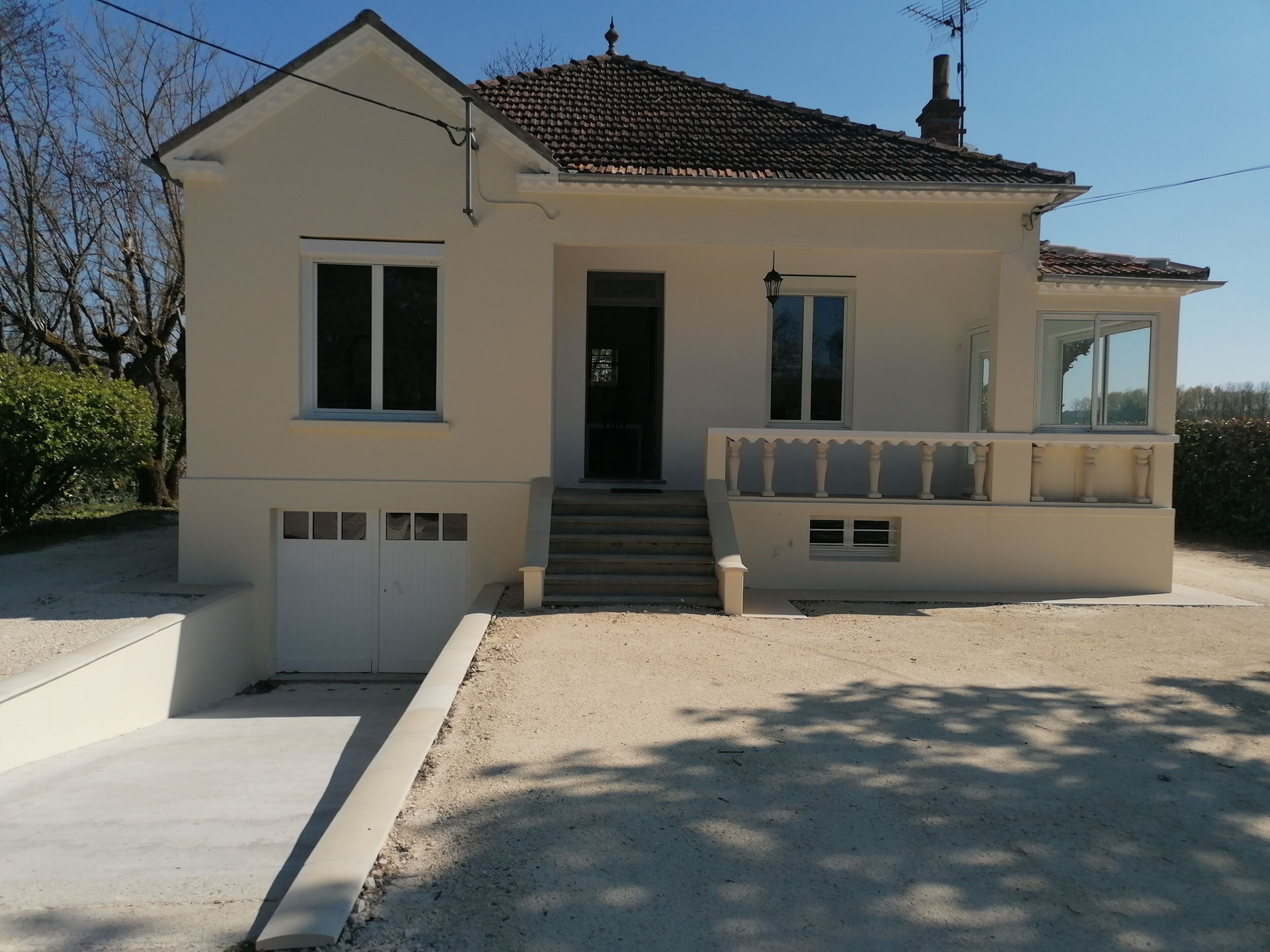 A two-story house with a tiled roof, a front porch with a bench, and a visible garage door.