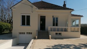 Ein zweistöckiges Haus mit Ziegeldach, einer Veranda mit Bank und einer sichtbaren Garagentür.