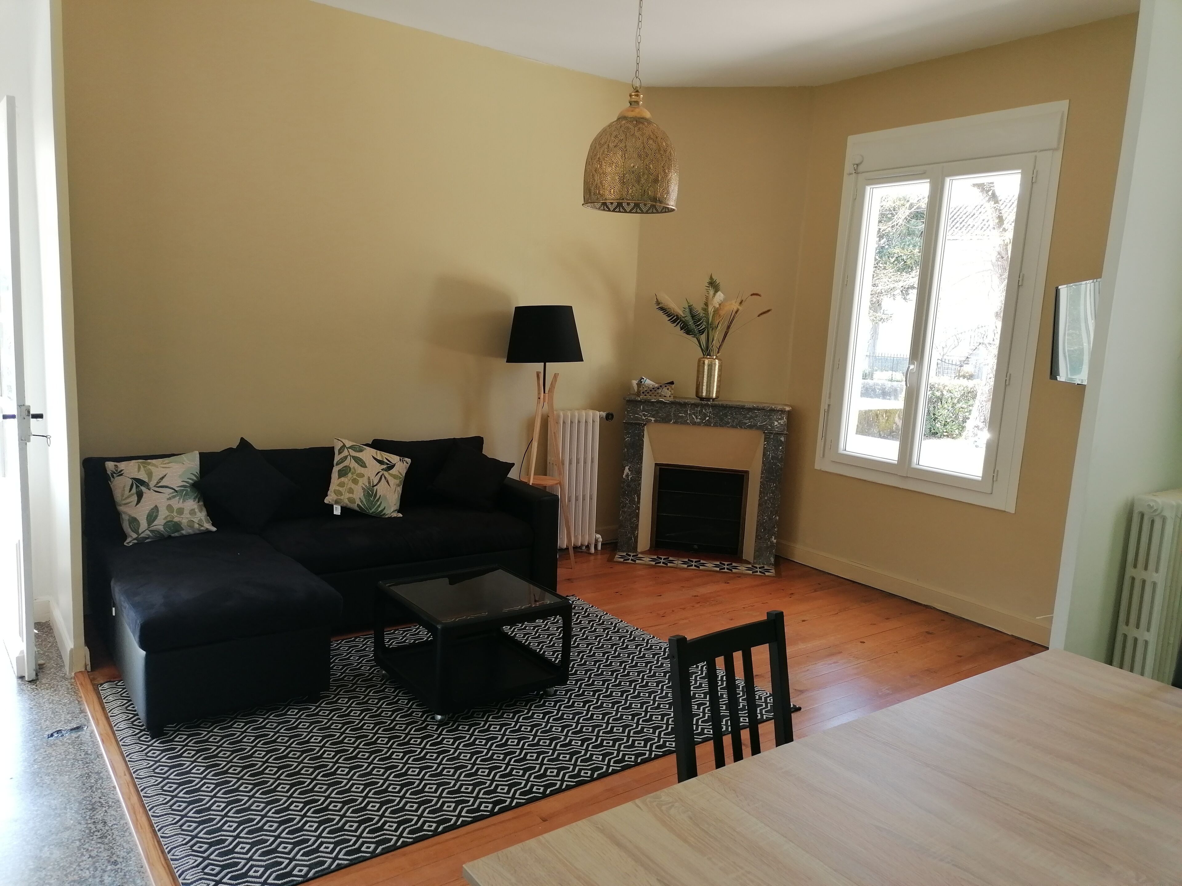 Ein Wohnzimmer mit schwarzem Sofa, Couchtisch, Kamin und Esstisch.