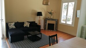 Ein Wohnzimmer mit schwarzem Sofa, Couchtisch, Kamin und Esstisch.