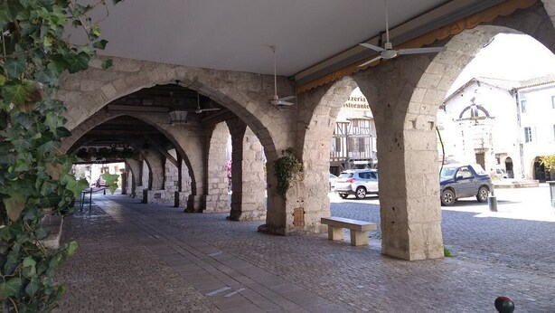 Ein überdachter Außenweg mit Steinbögen, einer Bank und einem Blumentopf.