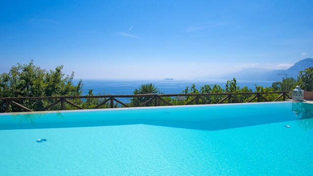 A clear blue pool with a wooden deck and a view of the ocean. - Art & Sea Boutique Villa (Praiano)