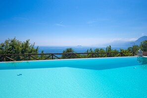 Ein klares, blaues Schwimmbecken mit einer Holzterrasse und Blick auf den Ozean.