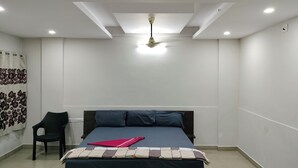 Ein Schlafzimmer mit Bett, Sessel, Deckenventilator und Wand mit blumigem Vorhang.