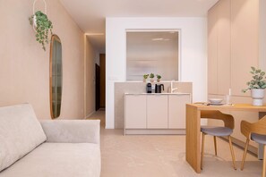 Ein modernes, minimalistisches Wohnzimmer mit einer Couch, einem Holzespeisetisch mit zwei Stühlen und einer Küchenzeile mit Schränken und Arbeitsplatte.