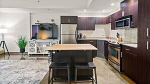 Una cucina moderna con mobili in legno scuro, elettrodomestici in acciaio inossidabile, un tavolo da pranzo in legno con due sedie e una piccola TV su un mobile bianco.