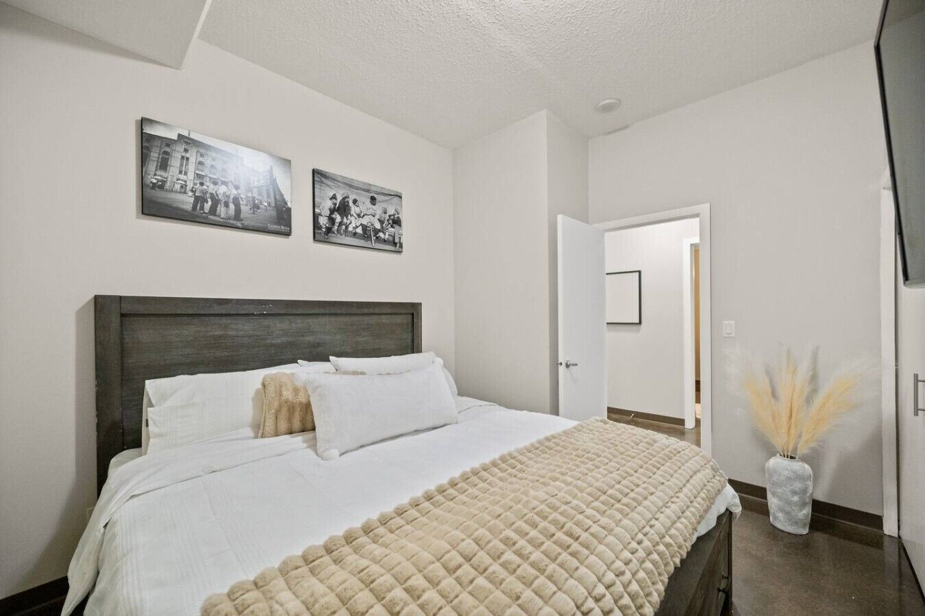 A bedroom with a bed, white walls, and two black-and-white photographs on the wall.