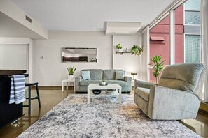 Ein modernes Wohnzimmer mit einem grauen Sofa, einem weißen Couchtisch und einem grauen Sessel. Es gibt ein großes Fenster mit roter Wand, einen kleinen Tisch mit einer Pflanze und einen Spiegel an der Wand.