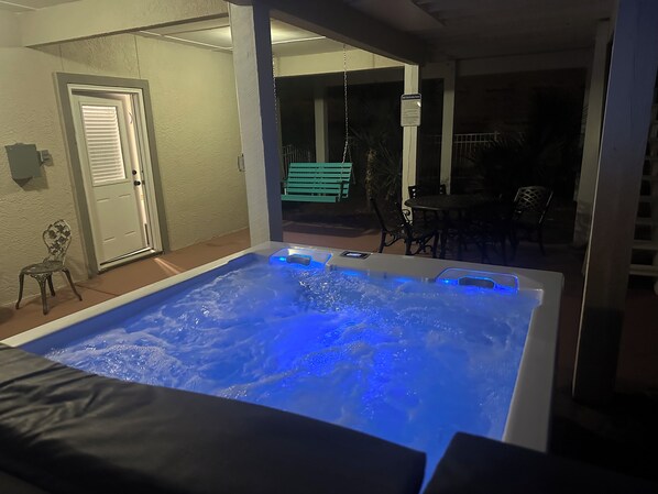 Un bain à remous avec un éclairage bleu, une porte et un espace extérieur aménagé avec des chaises et une table.