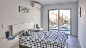Un dormitorio con una cama grande, una mesita de noche, una lámpara y una ventana con vista a la calle.