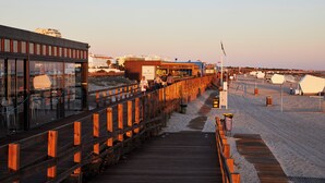 Un paseo marítimo de madera que lleva a una zona de playa con edificios y una bandera.