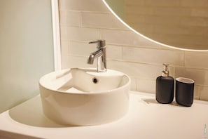 Ein Badezimmer mit einem weißen Waschbecken, einem Chrom-Wasserhahn und zwei schwarzen Seifenspendern auf einer weißen Arbeitsfläche.