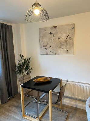 Spiseområde med bord, stole, en pendel, et billede og en plante.