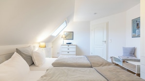 Ein Schlafzimmer mit Bett, Nachttisch, Lampe, Kommode und Schreibtisch mit Stuhl.