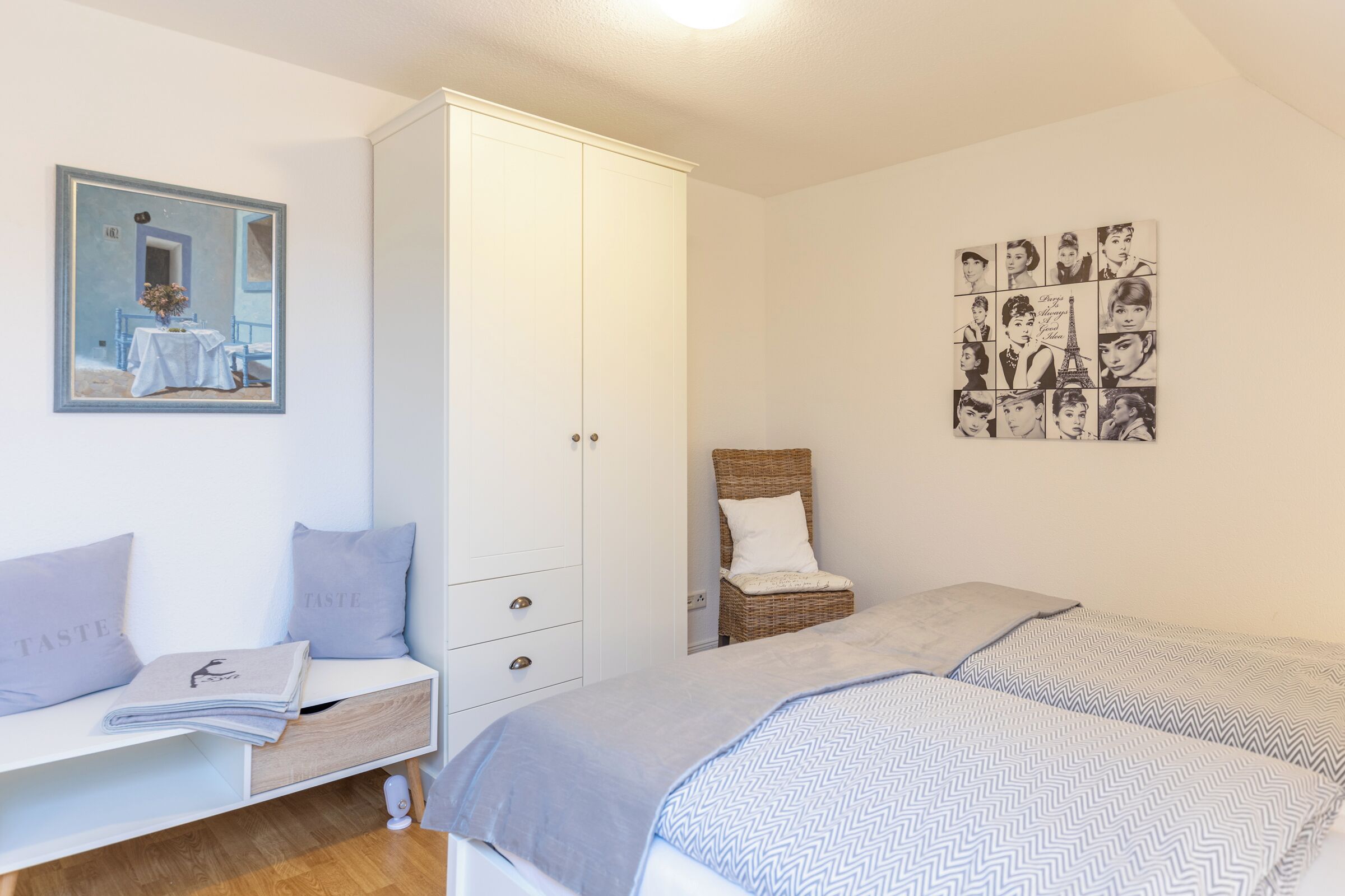 A bedroom with a bed, a wardrobe, a chair, and a wall with a collage of photos.