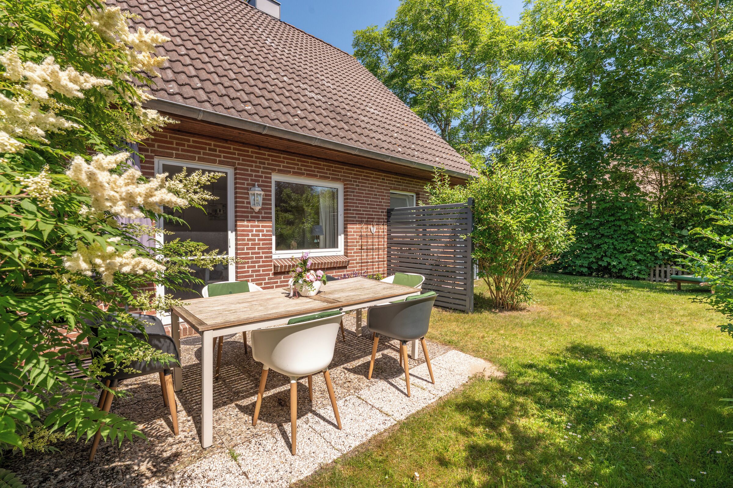 Ein Ziegelhaus mit einem Ziegeldach, einem Patio-Tisch mit Stühlen und einem Garten.
