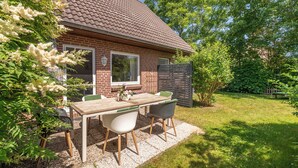 Ein Ziegelhaus mit einem Ziegeldach, einem Patio-Tisch mit Stühlen und einem Garten.