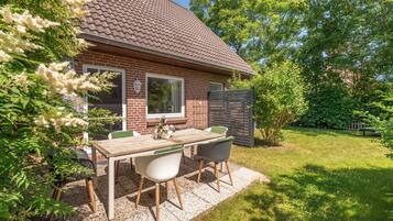 Ein Ziegelhaus mit einem Ziegeldach, einem Patio-Tisch mit Stühlen und einem Garten.