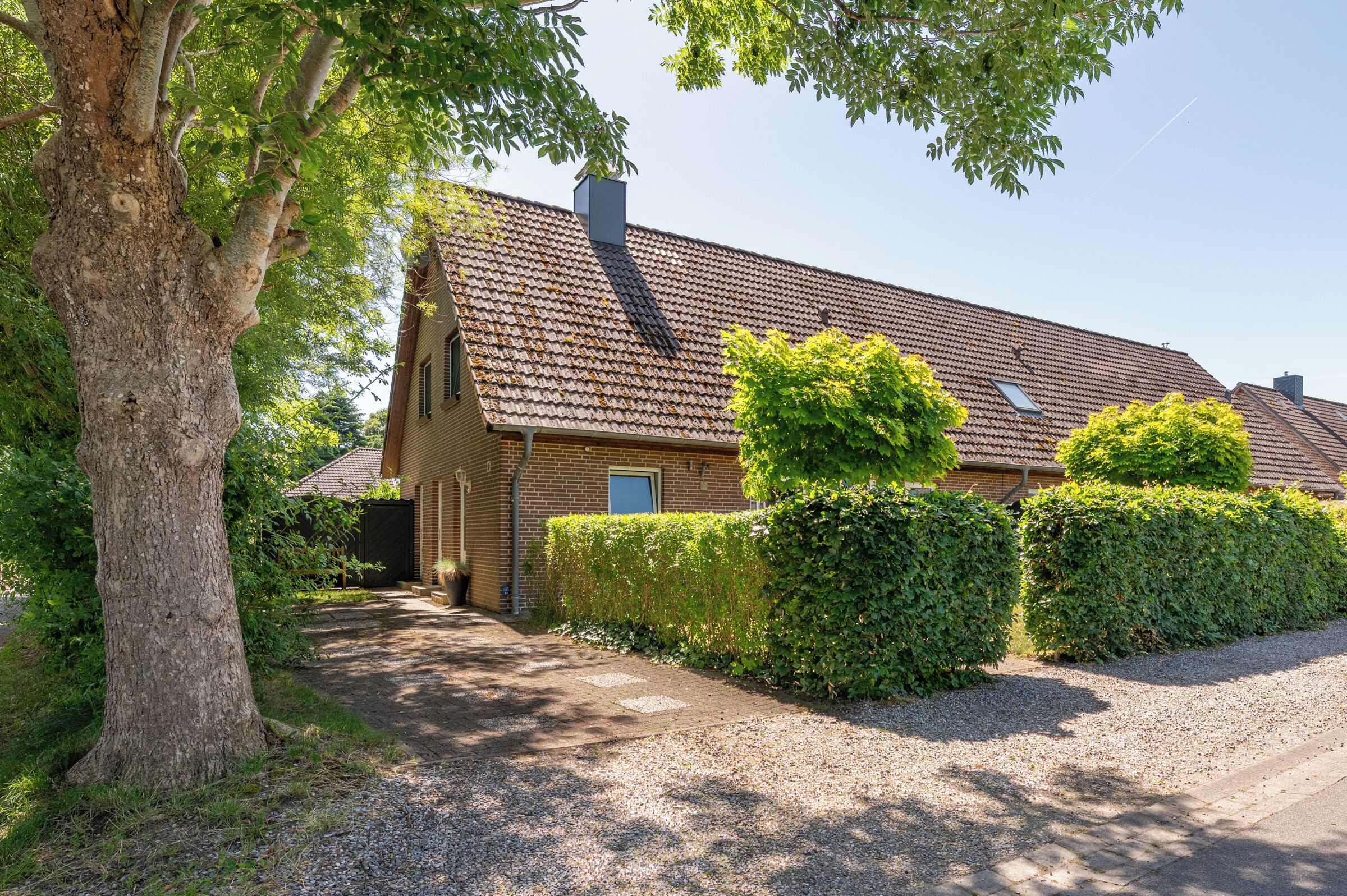 Ein Haus mit Kiesauffahrt, einem großen Baum und gepflegten Hecken.