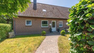 A brick house with a tiled roof, a paved driveway, and a small front yard with a bush and a potted plant.