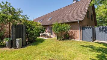 Ein Haus mit einem Ziegeldach, einem eingezäunten Garten und einer kleinen Terrasse.