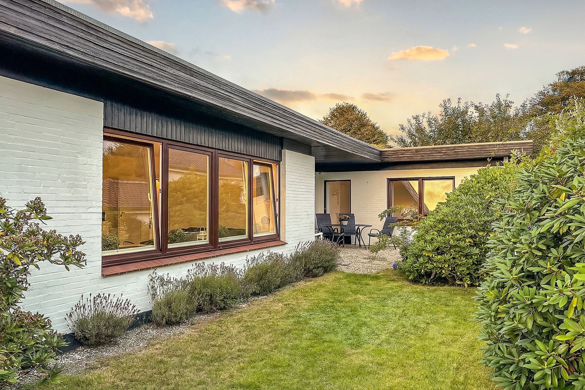 Ein modernes Haus mit weißer Fassade, großen Fenstern und einem gepflegten Garten.