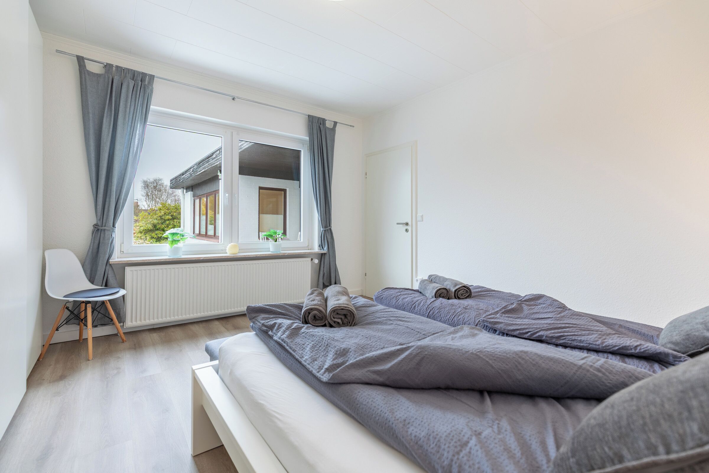 Et soveværelse med to senge, en stol, et vindue med gardiner og en radiator.