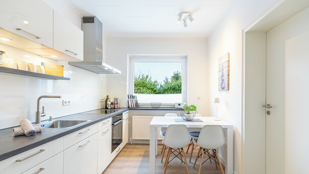 Una cocina moderna con armarios blancos, encimera negra y ventana con vistas a zonas verdes.