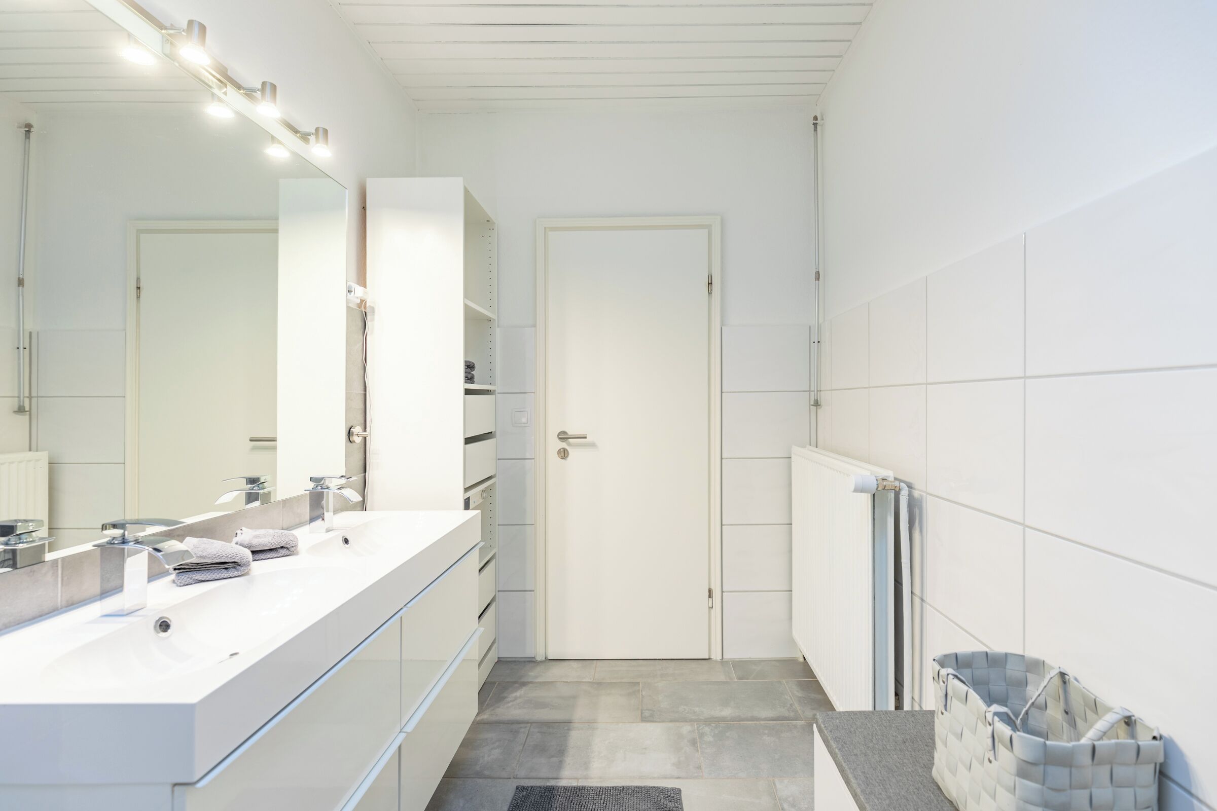 A modern bathroom with a white vanity, a large mirror, and a door.