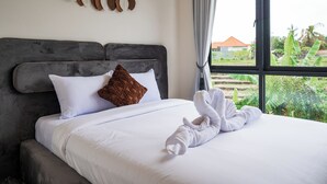 A neatly made bed with white and brown pillows, a grey headboard, and a towel on the bed. - Bohemia Villa by Betterplace (Canggu)