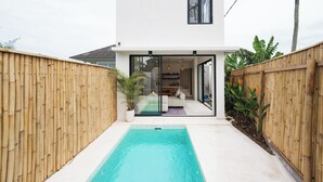 A modern house with a swimming pool, glass doors leading to a living area, and a bamboo fence. - Bohemia Villa by Betterplace (Canggu)