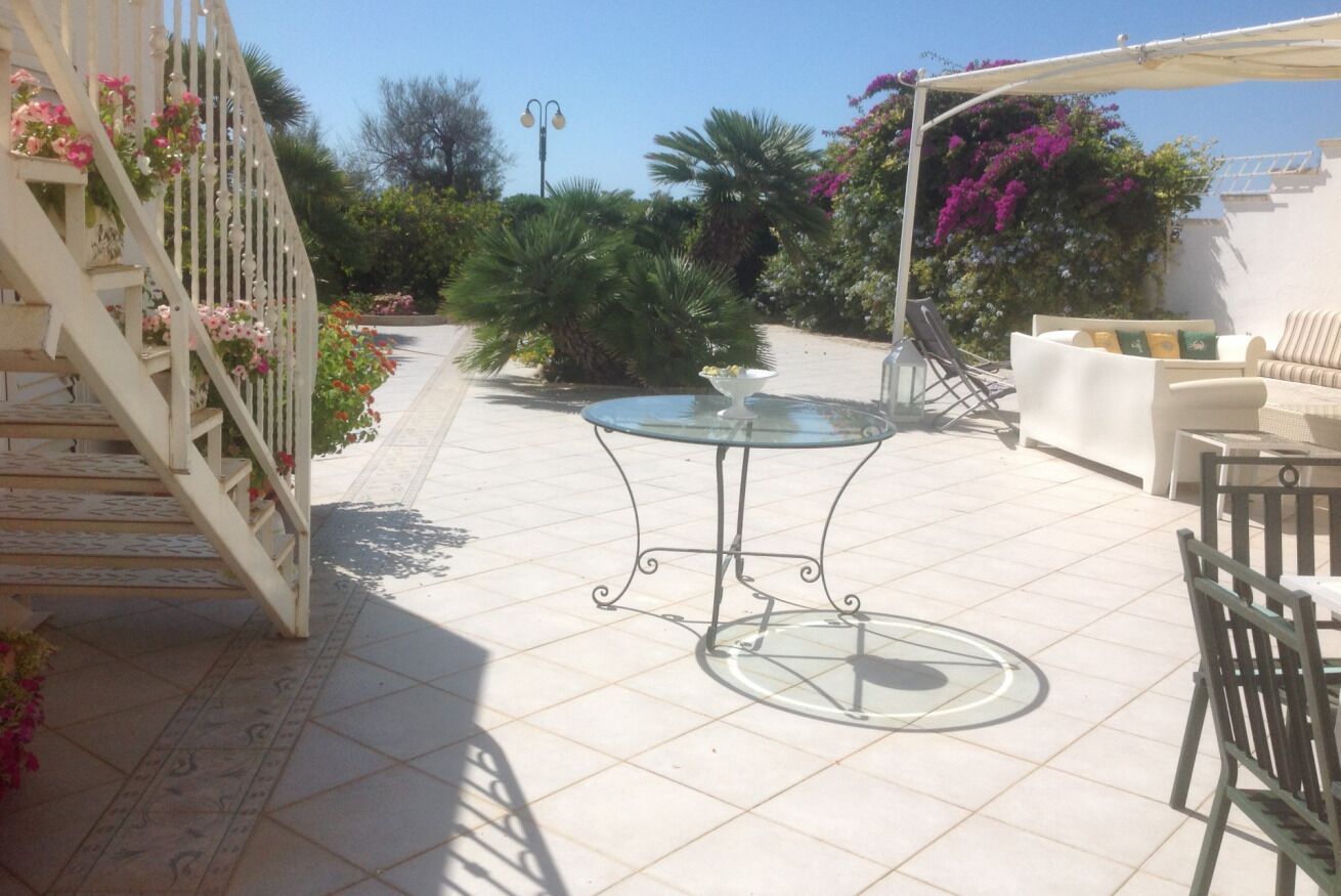 Un patio con mesa y sillas de vidrio, rodeado por una cerca blanca adornada con flores.