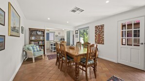Uma sala de jantar com uma mesa e cadeiras de madeira, uma estante e uma porta que dá para outro cômodo.