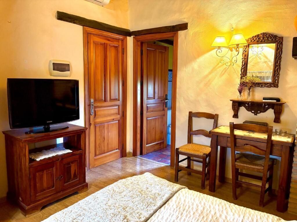 Une pièce comprenant un téléviseur posé sur un meuble en bois, un bureau avec deux chaises et un miroir agrémenté d’appliques murales.