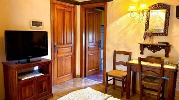 Une pièce comprenant un téléviseur posé sur un meuble en bois, un bureau avec deux chaises et un miroir agrémenté d’appliques murales.