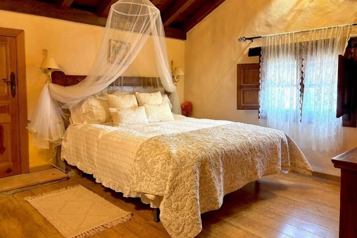 Une chambre à coucher avec un lit à baldaquin, un dais, un plancher en bois et une fenêtre avec des rideaux.