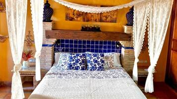 A bed with a canopy, a wooden headboard with blue tiles, and a small table with a vase.