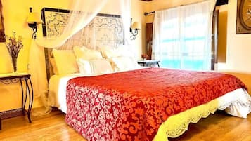 Une chambre à coucher avec un grand lit, une table de chevet, une lampe et une fenêtre avec des rideaux.