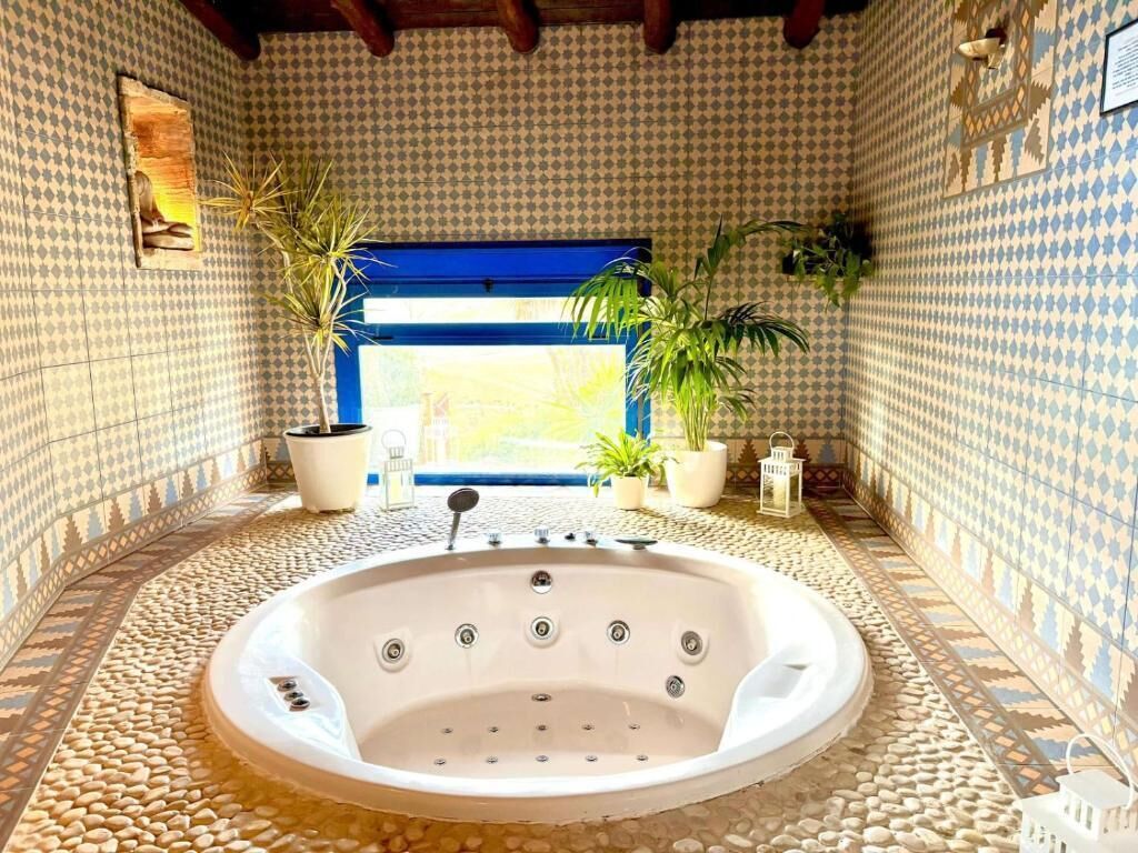 A spa room with a large bathtub, tiled walls, and potted plants.
