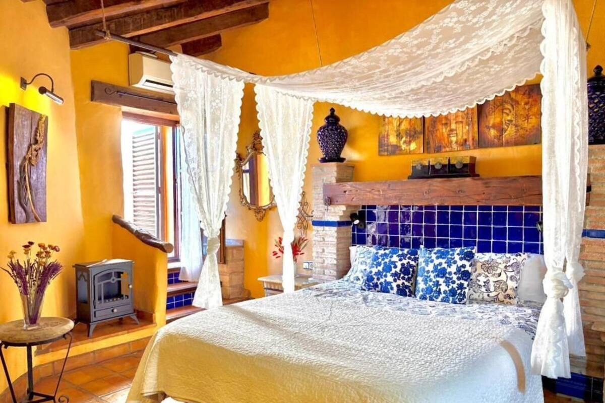 Une chambre à coucher avec un lit à baldaquin, un mur recouvert de carreaux et une petite table sur laquelle est posé un vase.