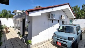 Um edifício pequeno, térreo, com fachada branca e telhado vermelho. Um SUV azul está estacionado em frente.