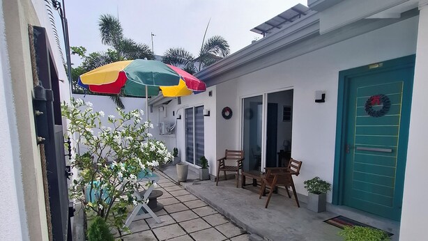 Um pátio com piso de azulejos, um guarda-sol colorido e uma porta decorada com uma guirlanda.