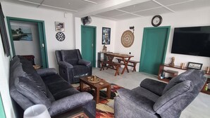 Uma sala de estar com sofás cinza, uma mesa de centro de madeira, um tabuleiro de xadrez e uma TV na parede.