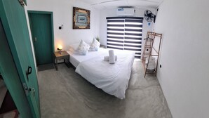 Quarto de hotel com cama, mesa de cabeceira, abajur e janela com persianas.