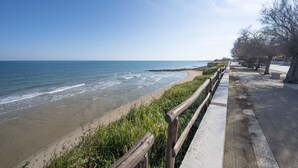 A coastal walkway with a wooden railing, a sandy beach, and a clear blue sky. - Apartment Lights (Avola)