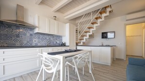 A modern kitchen with white cabinetry, a blue and white tiled backsplash, and a wooden staircase leading to a living area. - Apartment Lights (Avola)